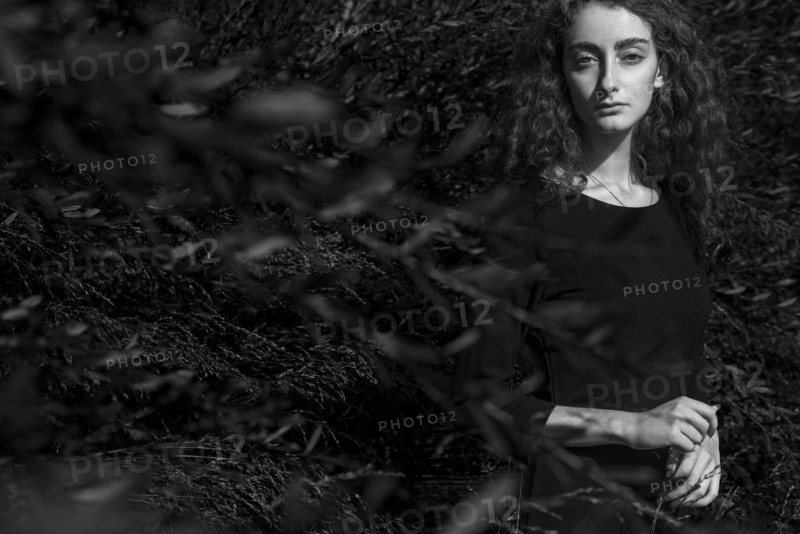 Serious Caucasian woman standing behind branches