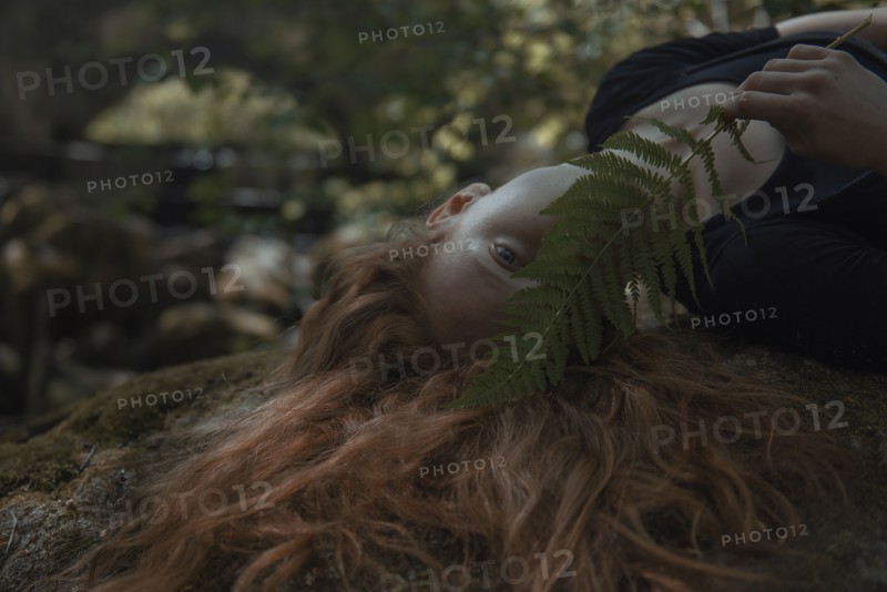 Caucasian woman with red hair hiding face behind leaf