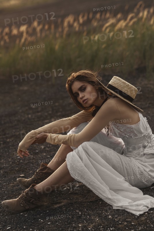Sexy Caucasian woman wearing white dress sitting in field