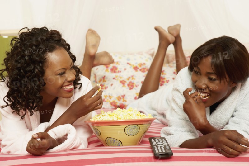 Two African women eating popcorn on bed