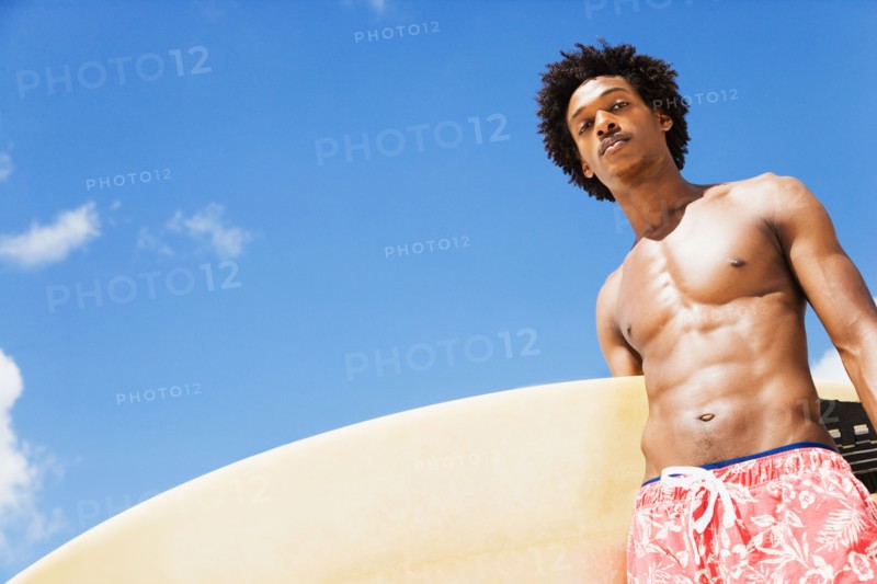 Serious African man holding surfboard
