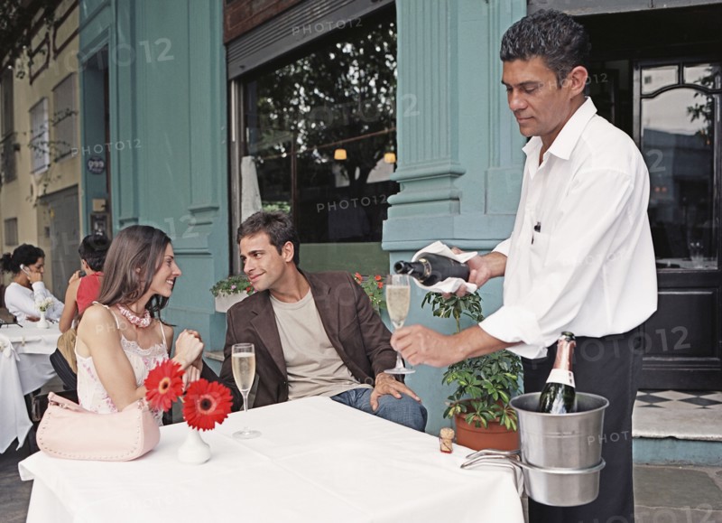 Hispanic couple having champagne at outdoor cafe