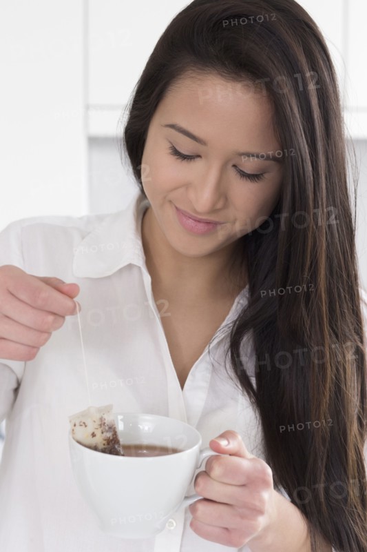 Mixed race woman having cup of tea in kitchen