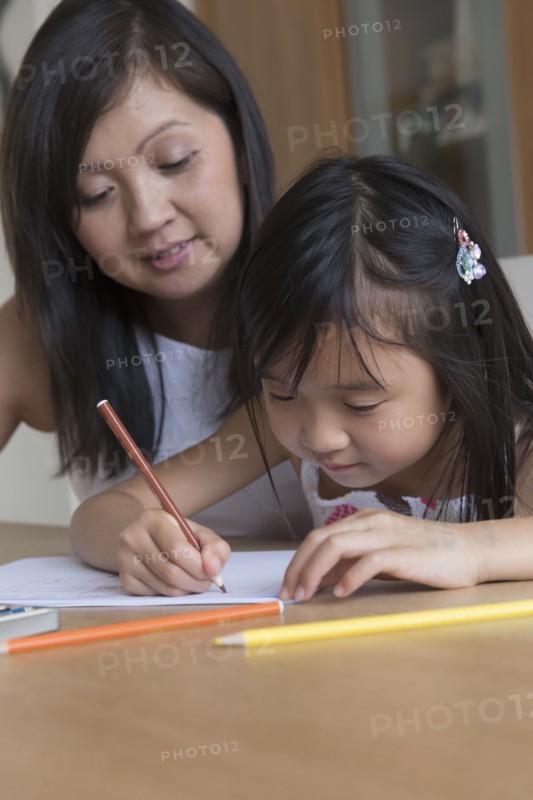 Asian mother watching daughter coloring