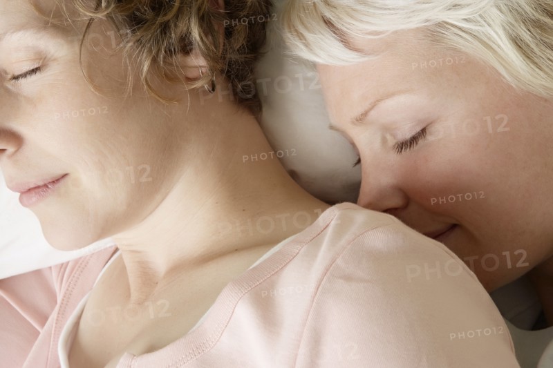 Caucasian lesbian couple sleeping on bed