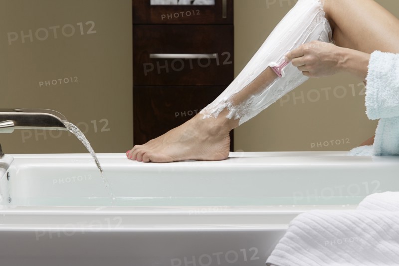 Caucasian woman shaving her legs at bathtub