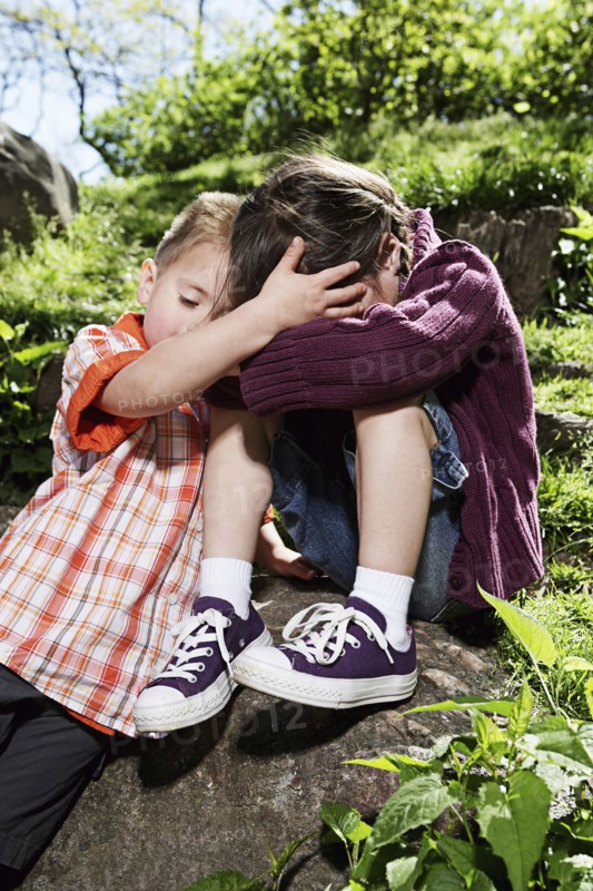 Mixed race boy comforting sister in park