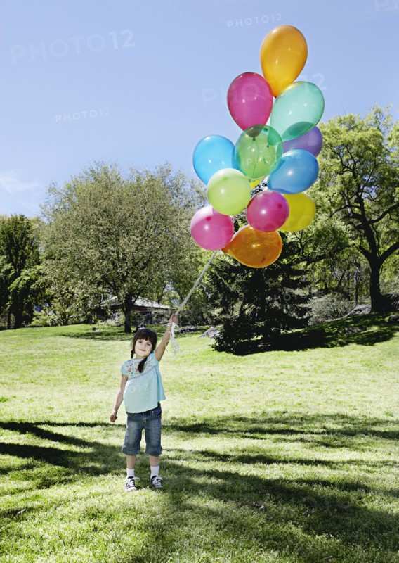 Mixed race girl holding bunch of balloons in park