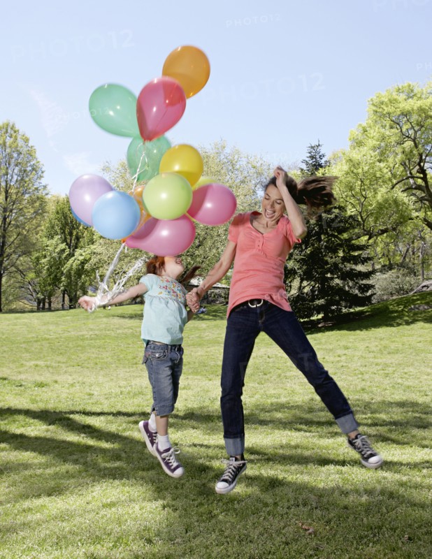 Mixed race mother and daughter holding balloons in park