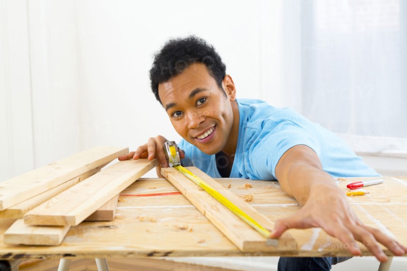 Mixed race carpenter measuring wood with tape measure
