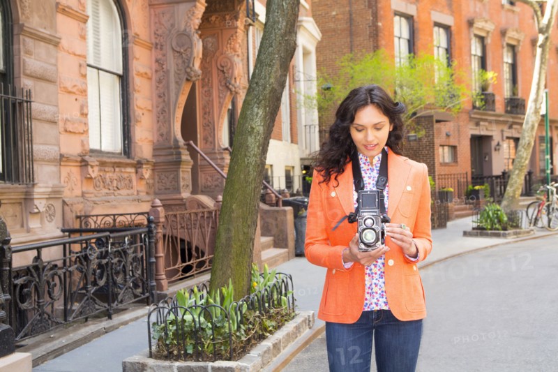 Mixed race woman taking pictures with vintage camera on city street