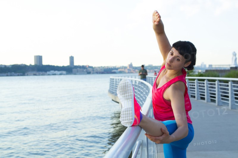 Mixed race woman stretching on urban waterfront railing