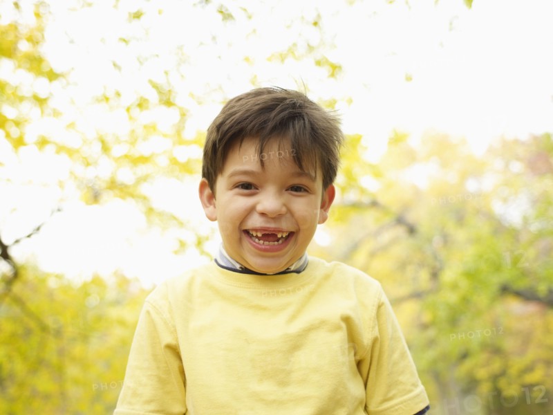 Toothless Hispanic boy grinning outdoors in autumn