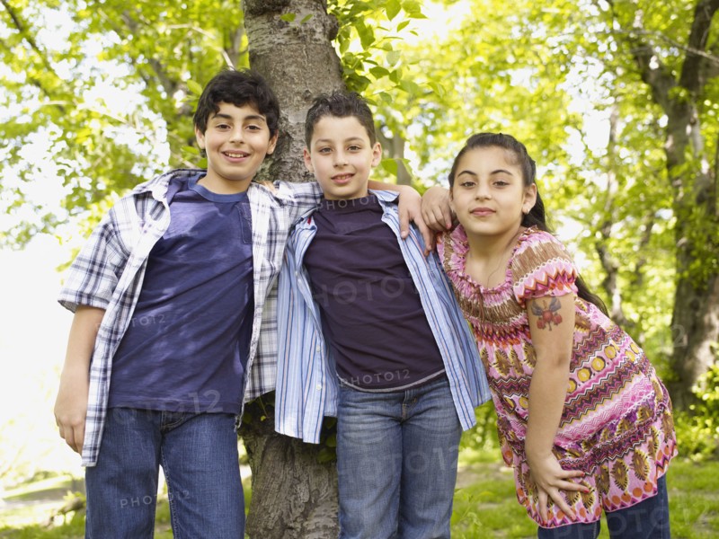 Mixed race boys and girl hugging in front of tree