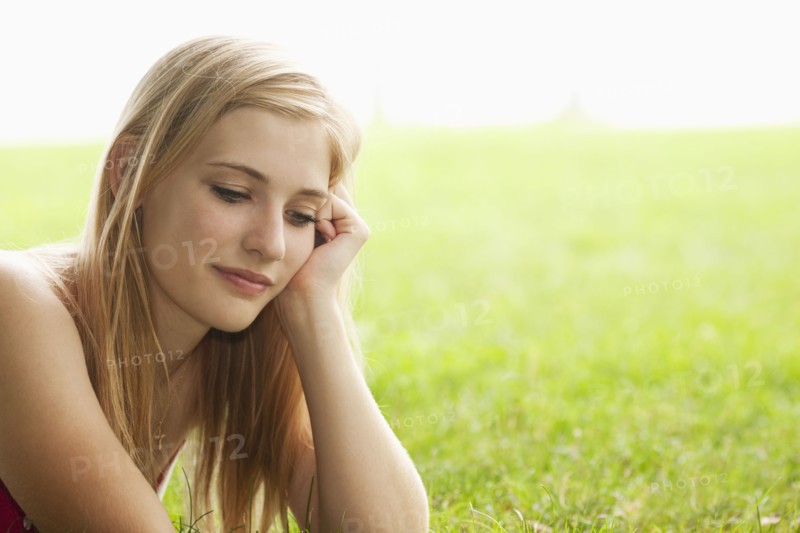 Serious Caucasian teenage girl sitting in grass