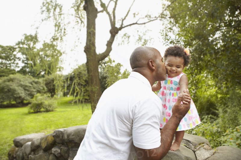 Mixed race father kissing daughter in park