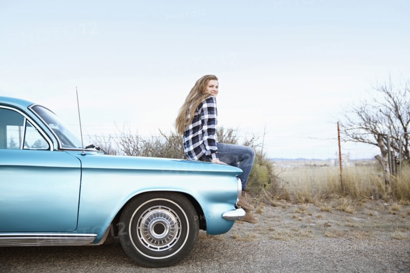 Smiling woman sitting on vintage car