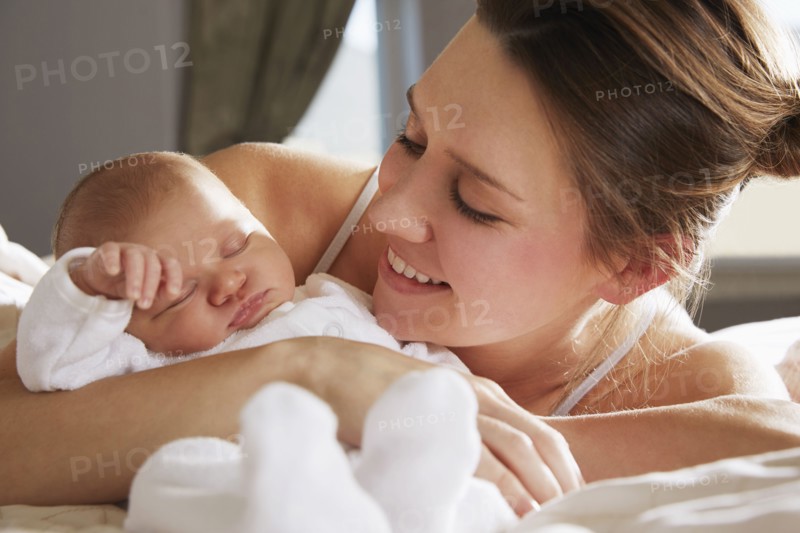Mother hugging newborn baby on bed