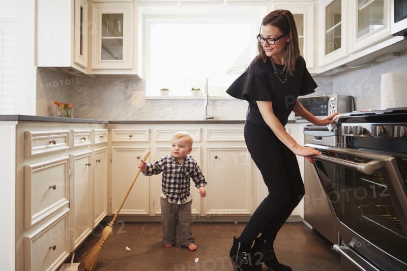 Caucasian mother and son holding broom kitchen