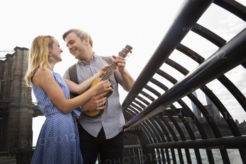 Caucasian couple playing ukulele on urban waterfront