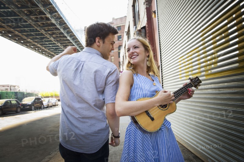 Caucasian couple playing ukulele in city