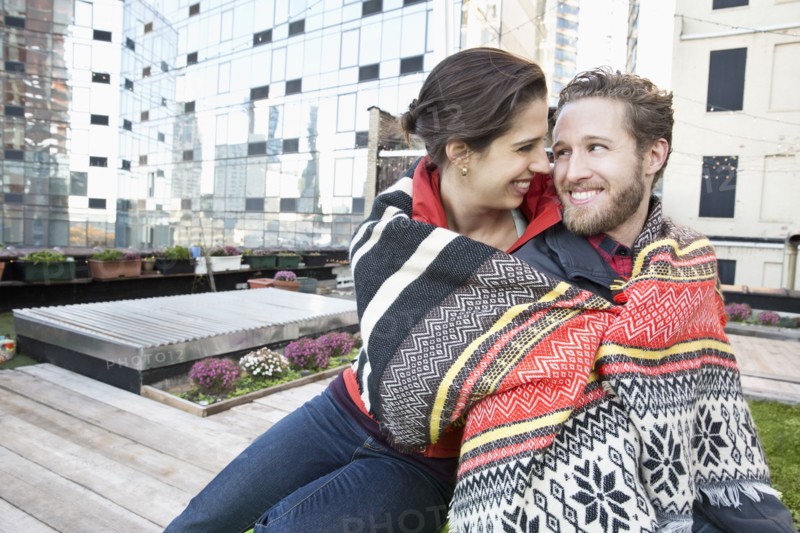 Couple wrapped in blanket on urban rooftop