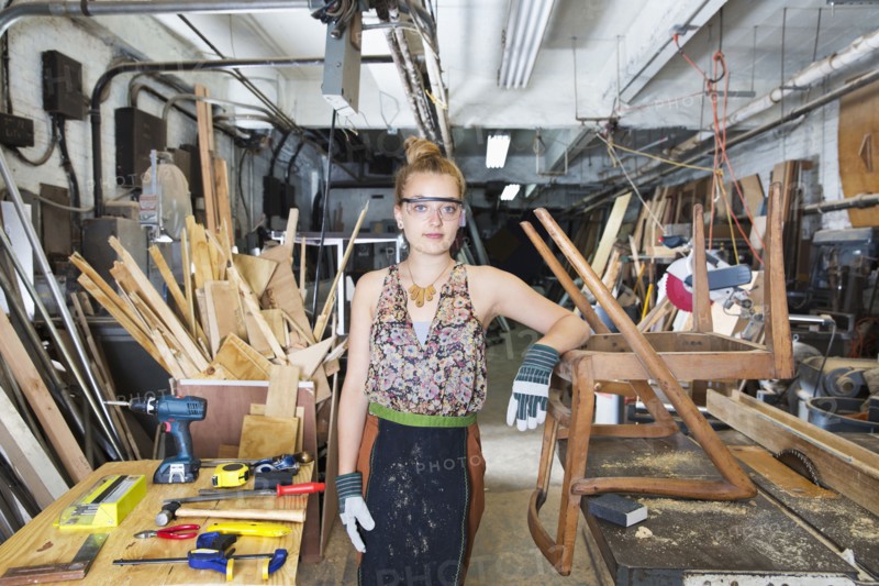 Caucasian woman leaning on wooden chair in workshop