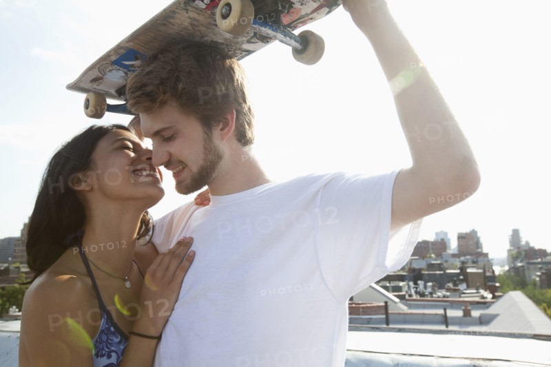 Mixed Race couple hugging on rooftop with skateboard