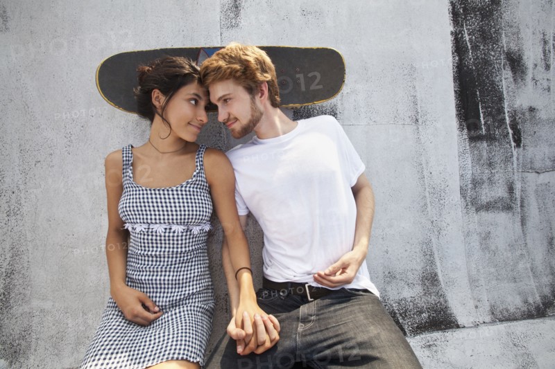 Mixed Race couple sitting on rooftop with skateboard