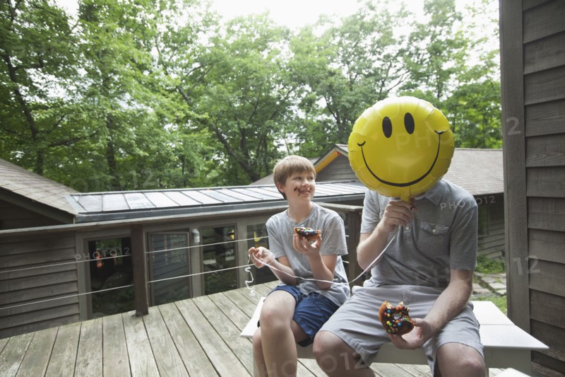 Caucasian father and son eating donuts with smiley face balloon