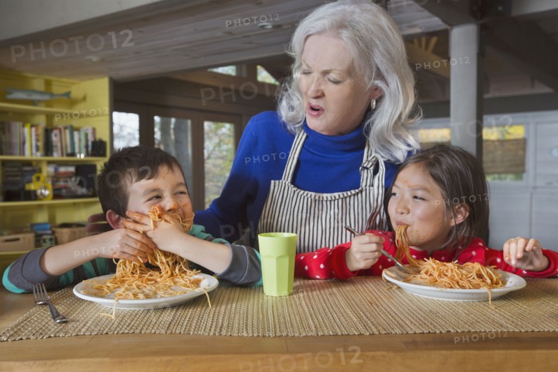 Grandmother watching grandson and granddaughter eat spaghetti