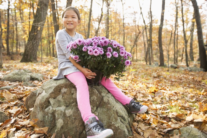 Smiling Mixed Race girls sitting on rock in autumn holding flowers
