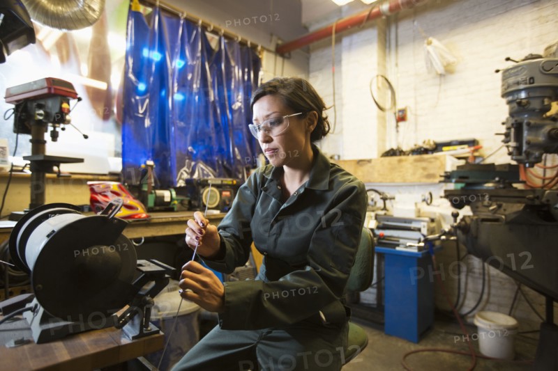 Mixed Race woman holding metal rod in workshop
