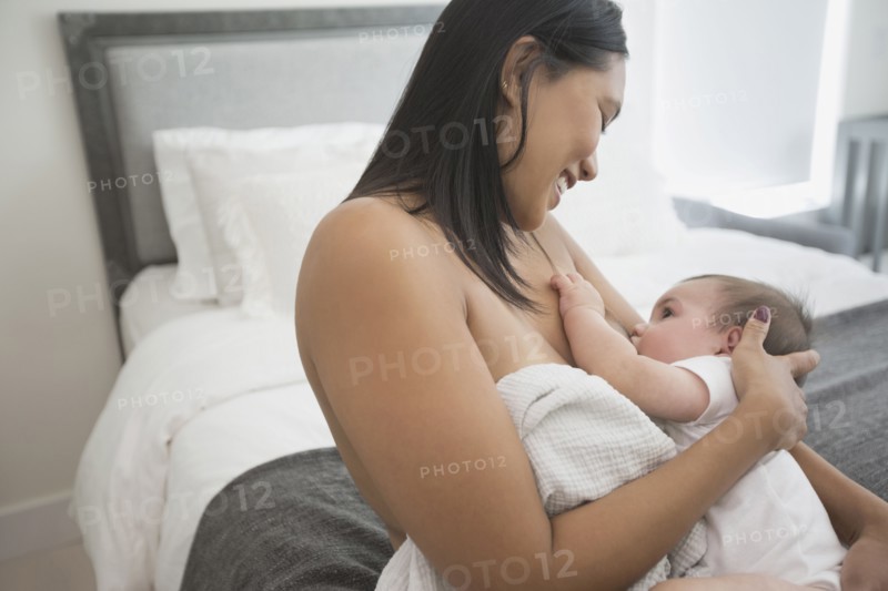 Woman sitting on bed breast-feeding baby son