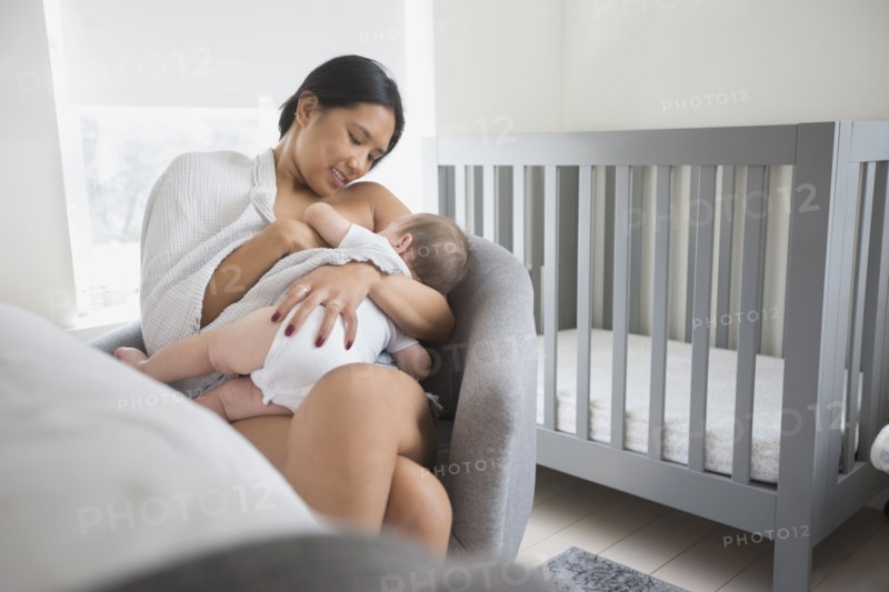 Woman sitting in armchair breast-feeding baby son