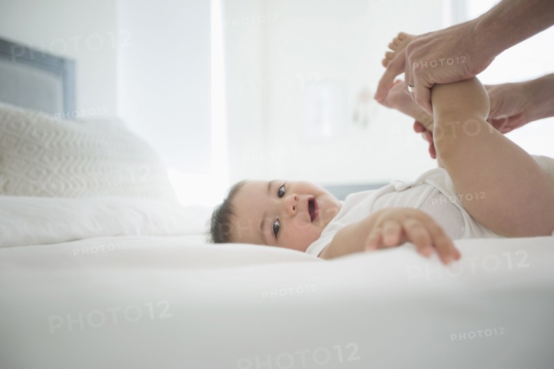 Father holding legs of baby son on bed