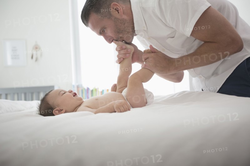 Father kissing feet of baby son on bed