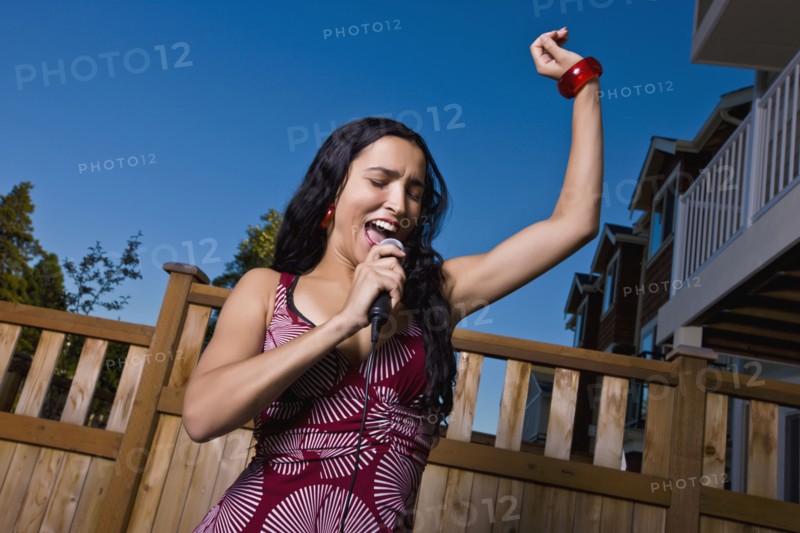 Hispanic woman singing karaoke in backyard