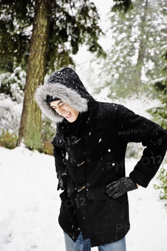 Mixed race man in hooded coat outdoors in snowfall