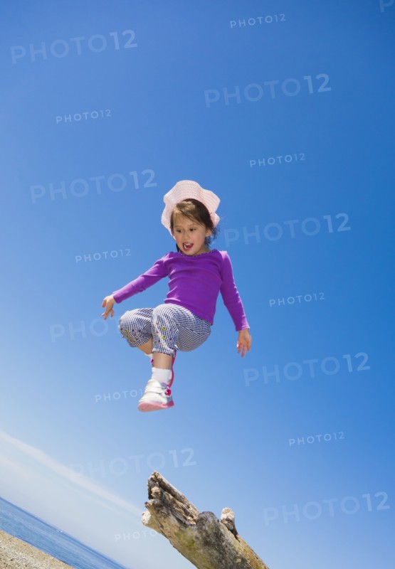 Low angle view of mixed race girl jumping from log on beach