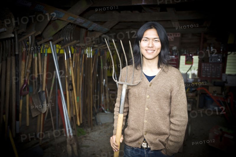 Japanese gardener holding pitchfork in barn