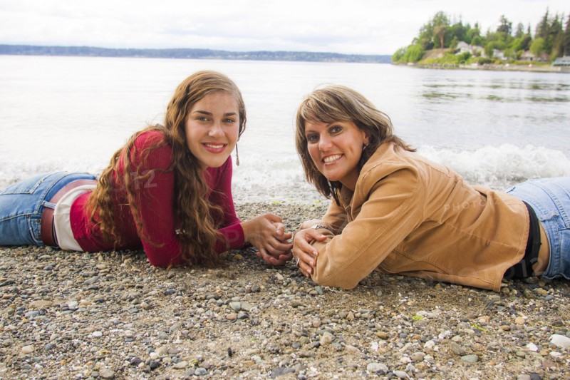 Smiling mother and daughter laying on rocky beach