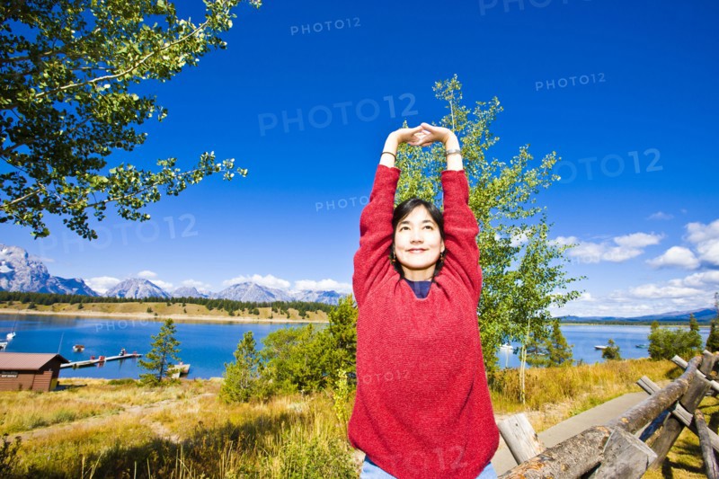 Smiling Japanese woman stretching arms near lake