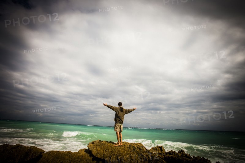 Caucasian man standing on rocks at ocean with arms outstretched