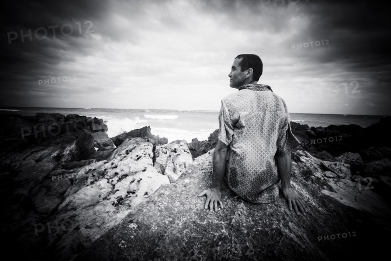 Pensive Caucasian man sitting on rocks at ocean