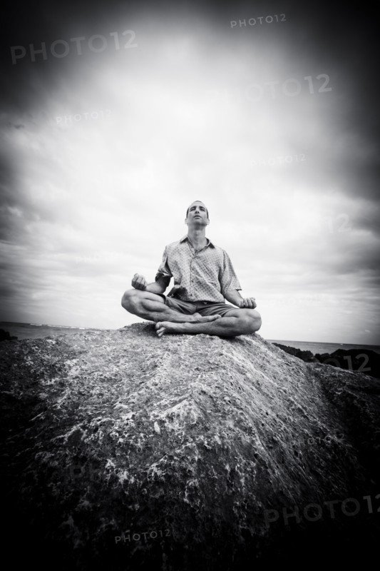 Caucasian man meditating on rocks at ocean