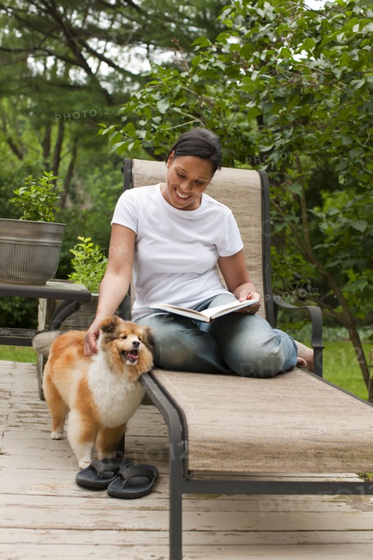 African American woman reading book and petting dog