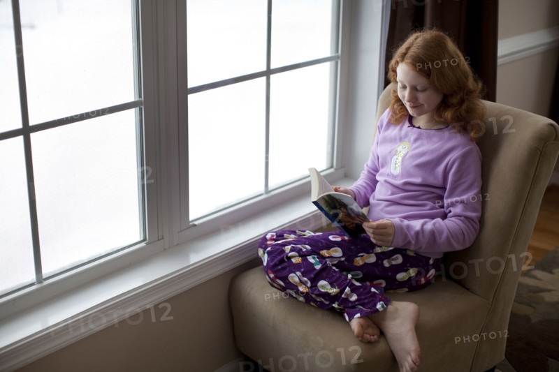 Caucasian girl reading on book near window