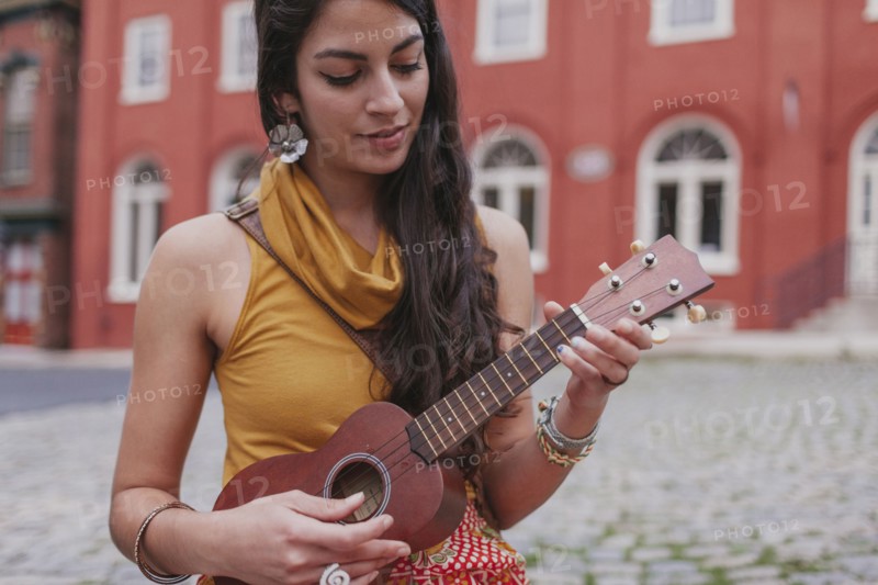 Mixed race woman playing ukulele on city street