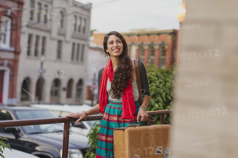 Mixed race woman carrying suitcase on city street